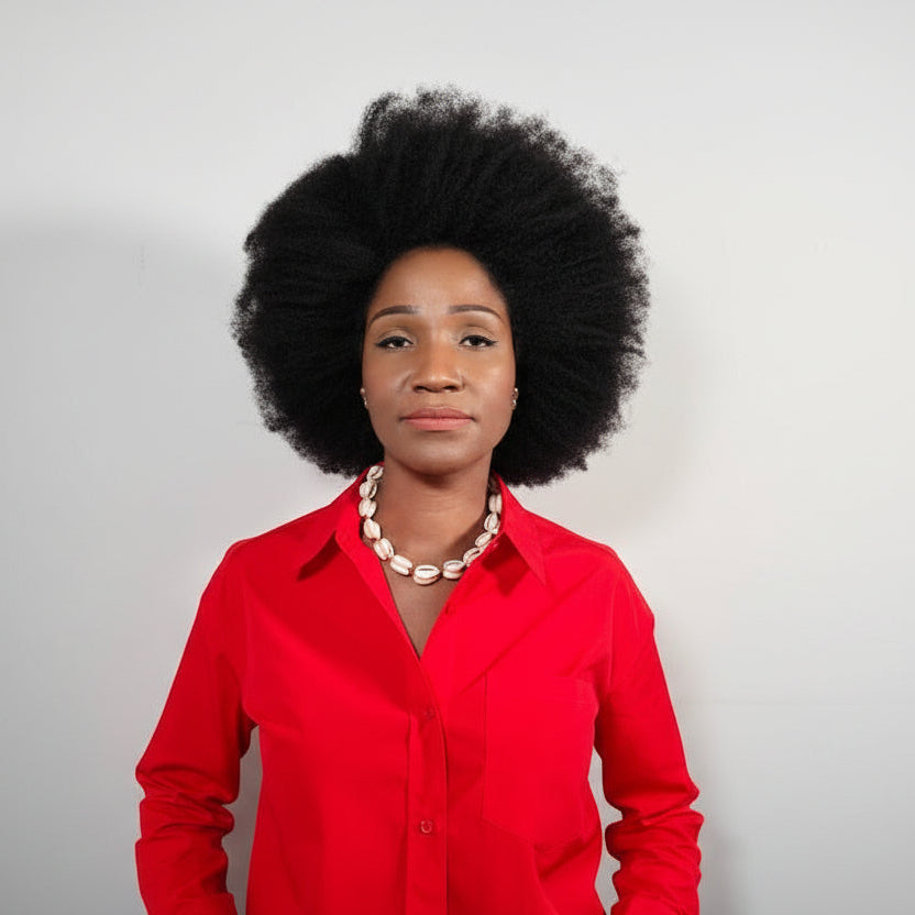 Woman wearing a red shirt with a short length cowrie shell necklace, she's standing against a plain white background