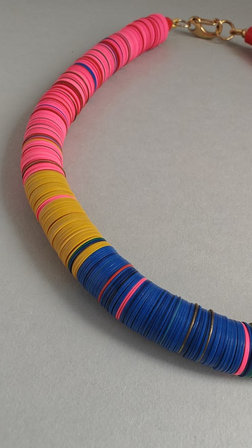 Close up of a colorful necklace with pink, yellow, and blue circular beads on a gray background