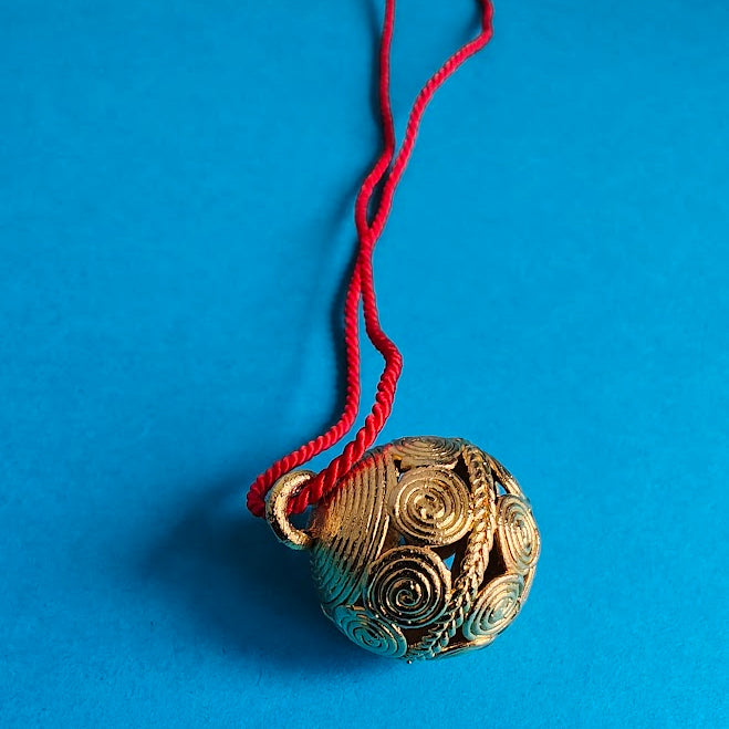 Decorative gold pendant with intricate patterns on a red string against a blue background