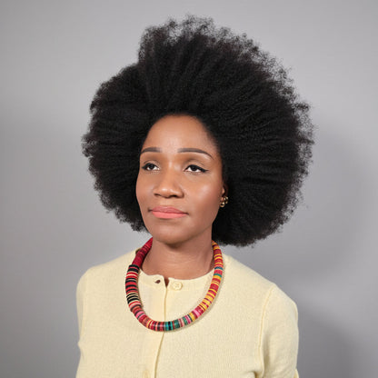 Woman with an afro wearing a colorful necklace against a plain background