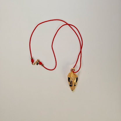 Gold cocoa pod pendant on a red string against a light gray background