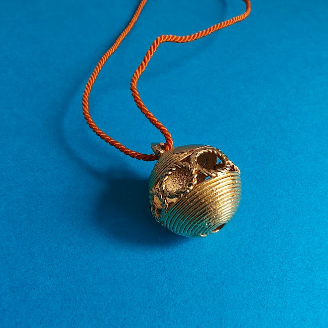 Gold pendant on an orange cord against a blue background