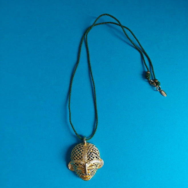 Gold African mask pendant on a green cord against a blue background