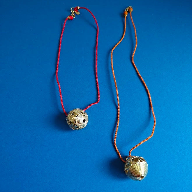 Two round textured brass pendents on coloured cord srting  on blue background