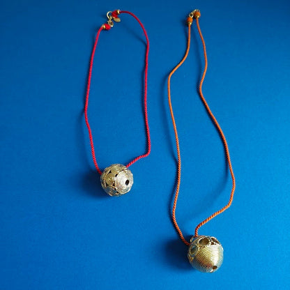 Two round textured brass pendents on coloured cord srting  on blue background
