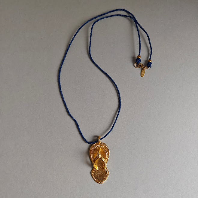 Gold pendant on a blue cord against a gray background