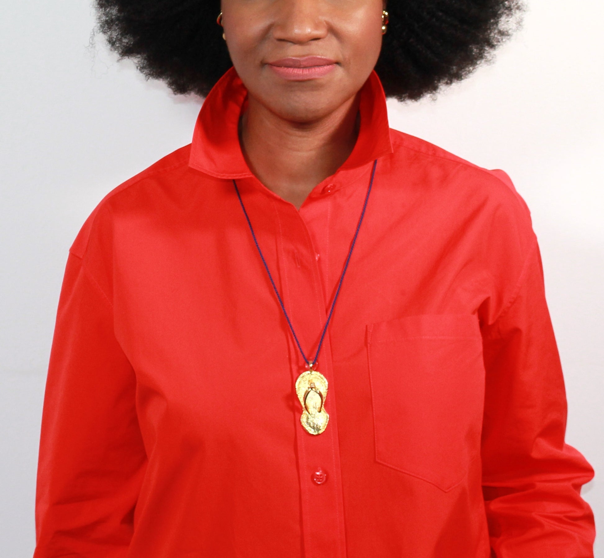 Person wearing a red shirt with a necklace featuring a slipper pendant.