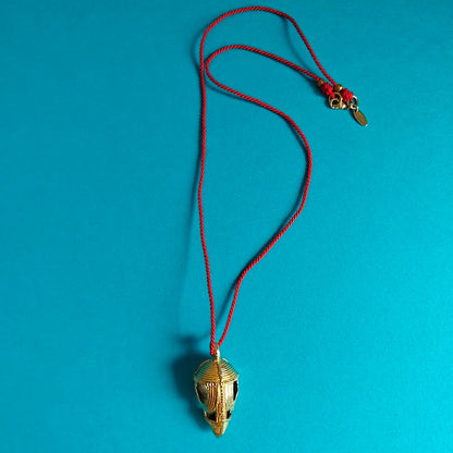 Gold cocoa pod pendant on a red cord against a blue background