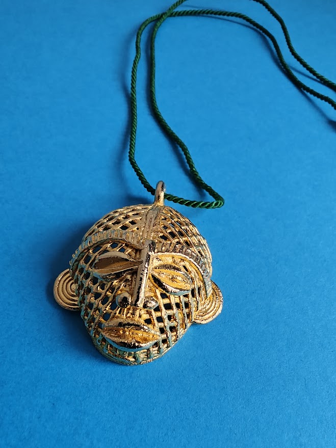 Decorative African mask pendant, with a green cord and on a blue background