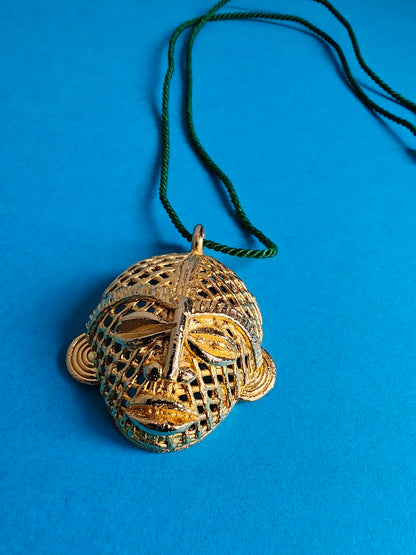 Decorative African mask pendant, with a green cord and on a blue background
