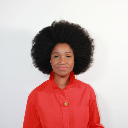Person wearing a gold ball pendent and a red shirt with a plain background