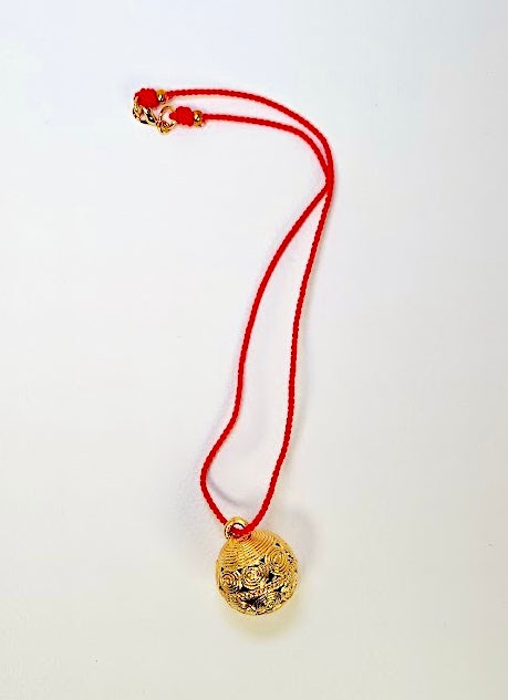 Gold pendant on a red string against a white background