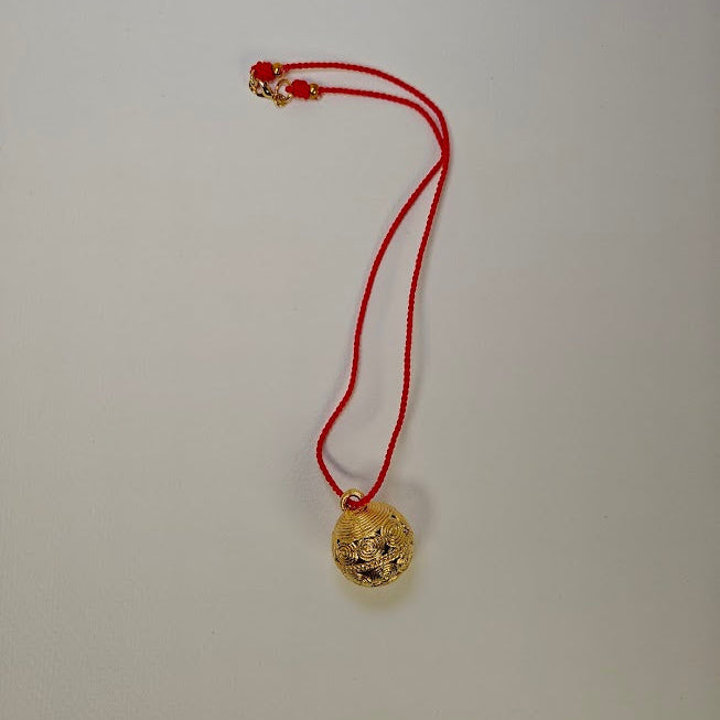Gold pendant on a red string against a plain background