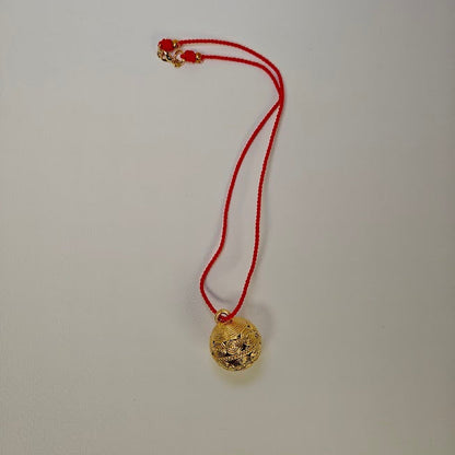 Gold pendant on a red string against a plain background