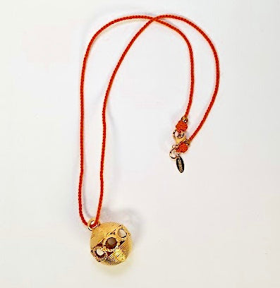 Necklace with a gold pendant on an orange cord against a white background