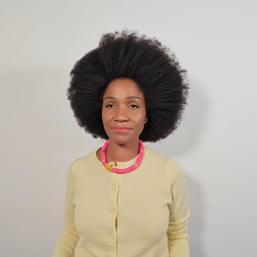 Woman wearing a light yellow cardigan with a pink necklace against a plain background