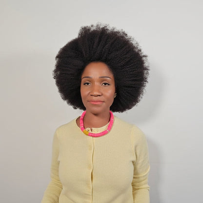 Woman wearing a light yellow cardigan with a pink necklace against a plain background