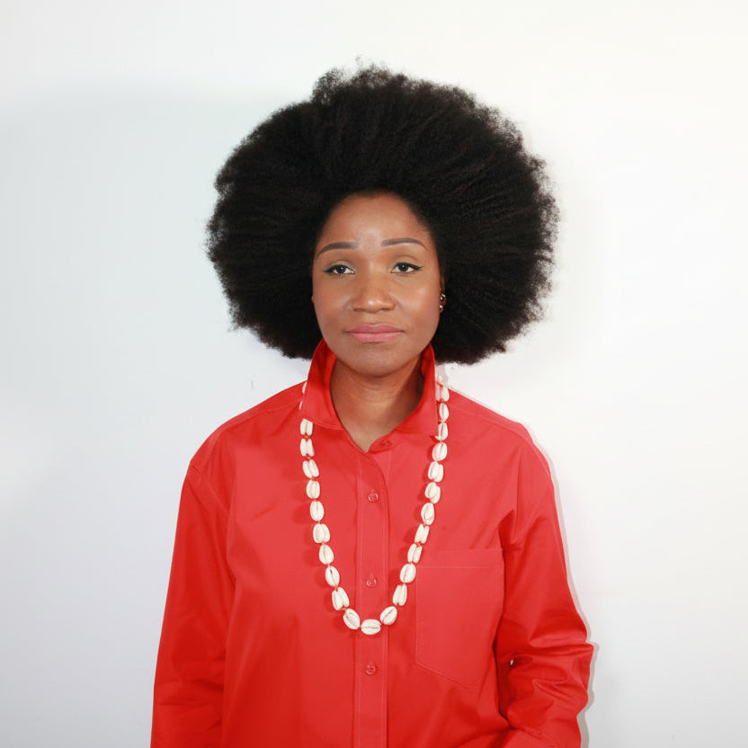 Person wearing a red outfit with a white cowrie shell necklace on a plain background