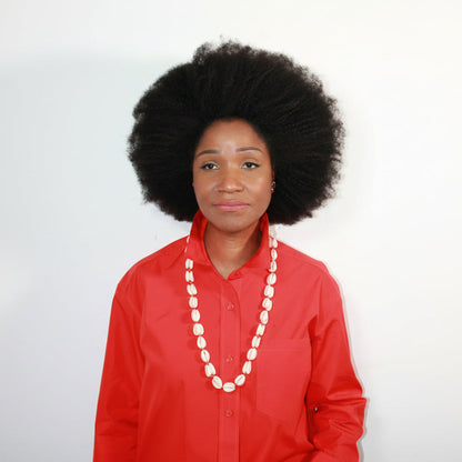Person wearing a red outfit with a white cowrie shell necklace on a plain background