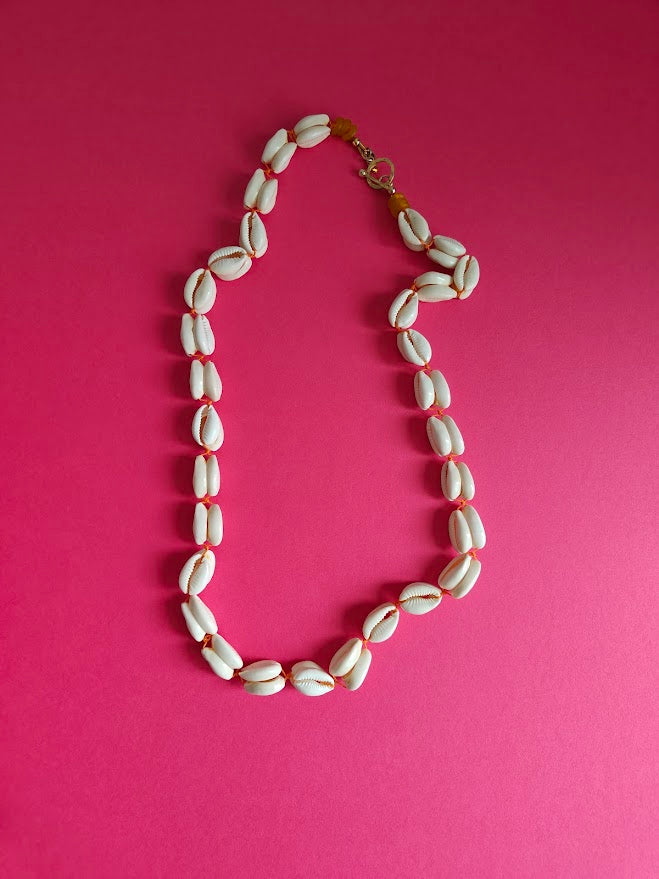 Long length cowrie shell and glass bead necklace on a pink background 