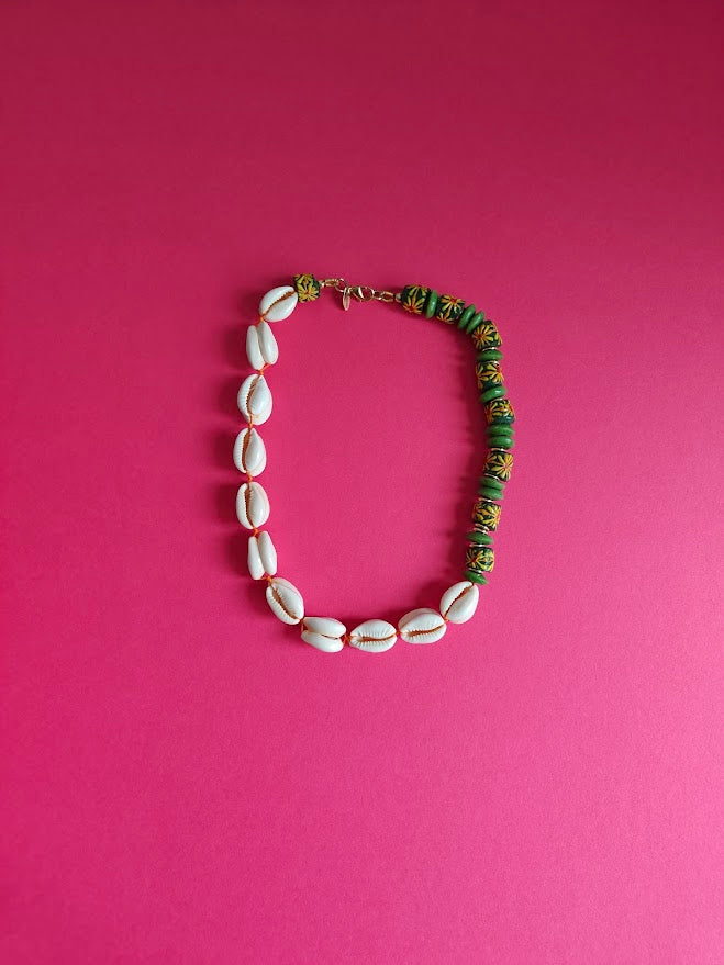 Necklace with cowrie shells and green floral design recycled glass beads  on a pink background