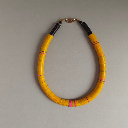 Yellow necklace with accents of  pink and black beads on a grey bbackground