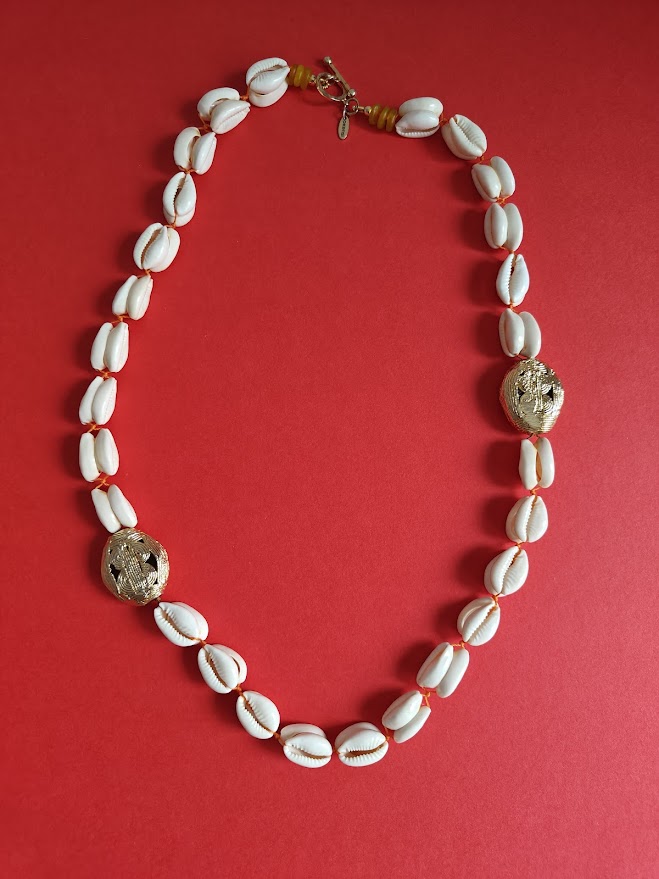 Long necklace with cowrie shell beads, large gold brass beads and accents of yellow recycle glass beads on a red background