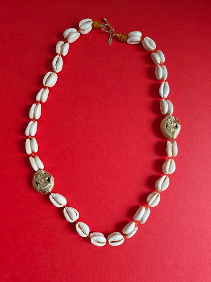 Long necklace with cowrie shell beads, large gold brass beads and accents of yellow recycle glass beads on a red background