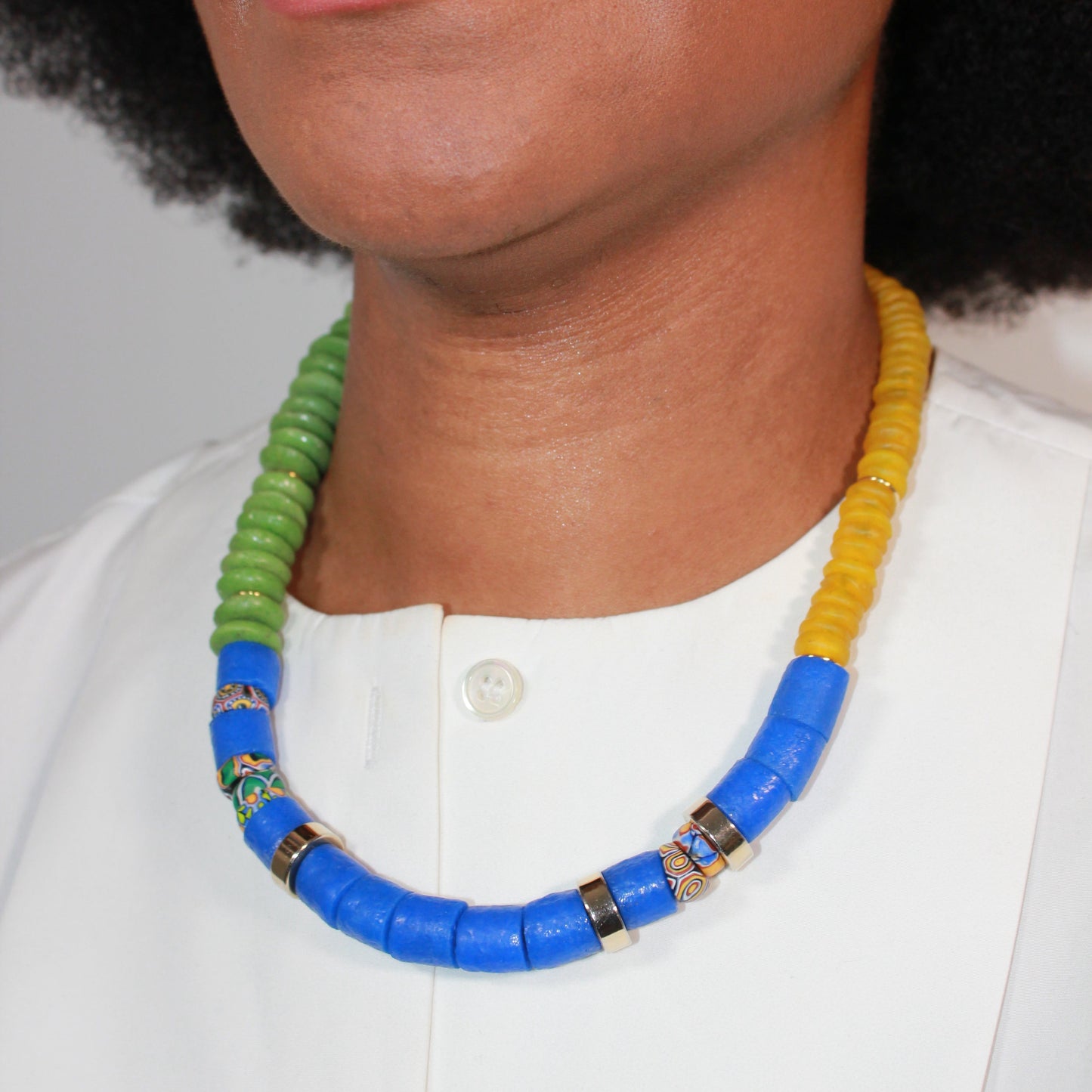 Necklace with blue, green, and yellow beads worn by a person against a neutral background