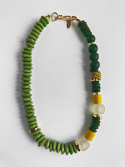 Necklace with green and yellow beads and gold accents on a light gray background
