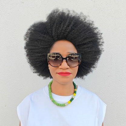 Woman with an afro wearing a beaded necklace, sunglasses and a white top against a light background