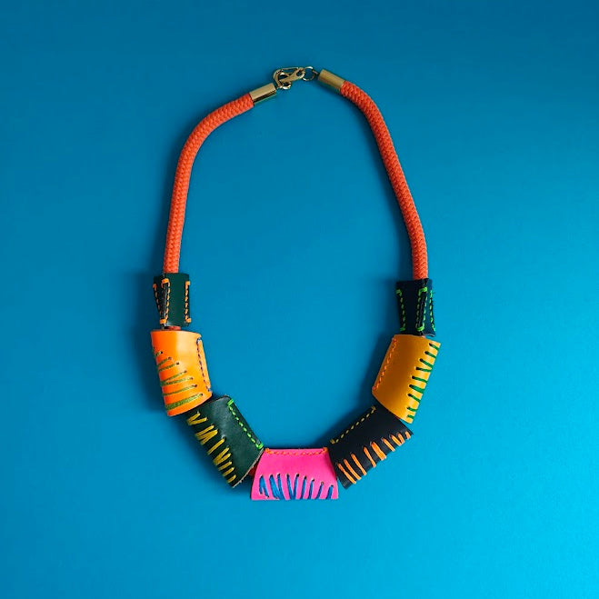 Neon orange rope and colourful geometric handcrafted leather beads necklace on a light gray background