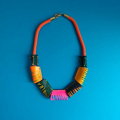 Neon orange rope and colourful geometric handcrafted leather beads necklace on a light gray background