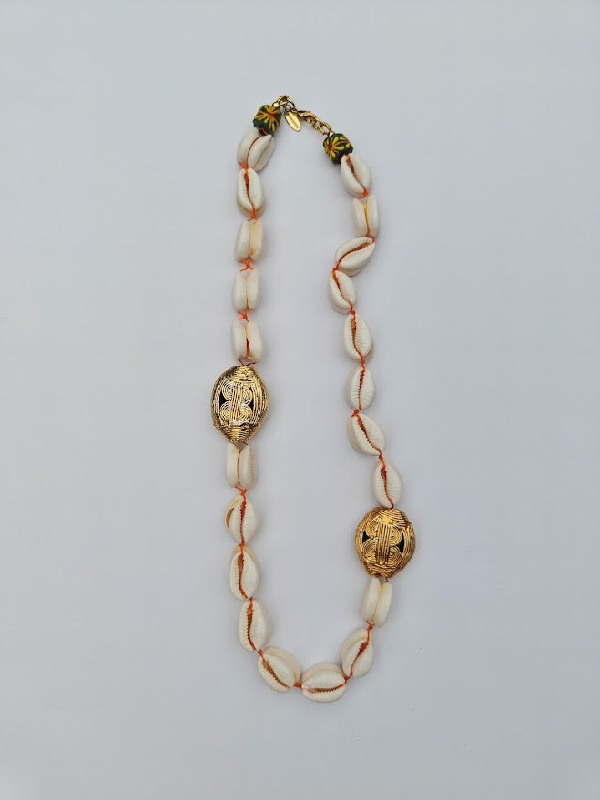 Long necklace with cowrie shell beads, large gold brass beads and accents of yellow recycle glass beads on a light gray background