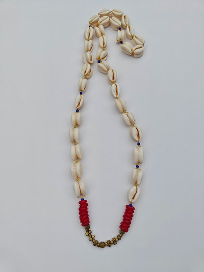 Long cowrie shell necklace with red and gold brass accent beads on a light gray background