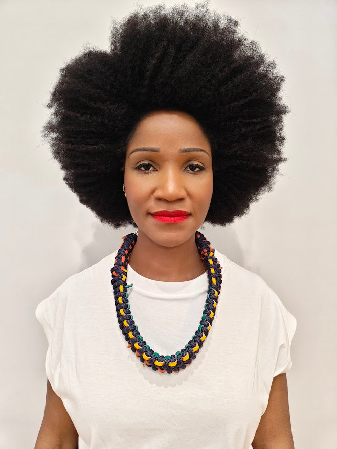 Person with an afro wearing a statement navy rope and leather necklace, with a white tee shirt