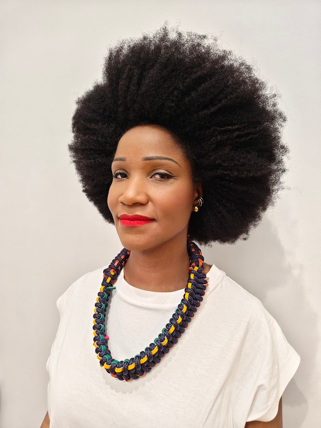 Person with an afro wearing a statement navy rope and leather necklace, with a white tee shirt