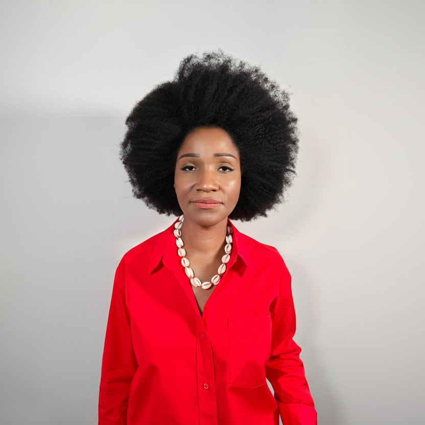 Woman wearing a red shirt with a  medium length cowrie shell necklace, she's standing against a plain white background