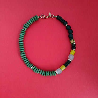 Beaded necklace with green, dark greeen, yellow, and gold plated beads on a red background