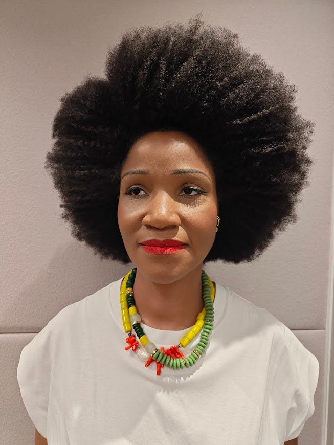 Woman with an afro wearing two colorful necklace against a neutral background