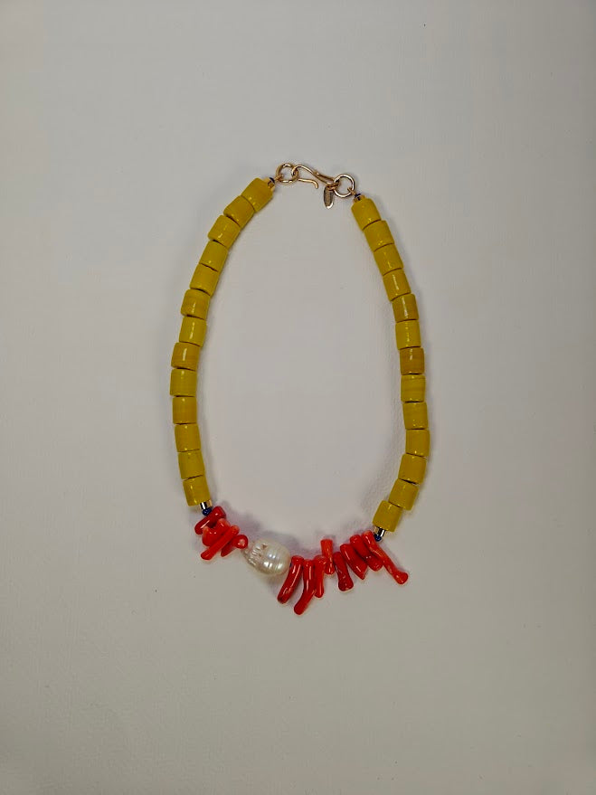 Necklace with yellow beads, freshwater baroque pearl and red coral-like elements on a light gray background