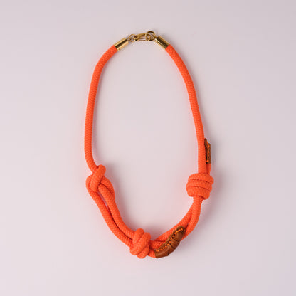Neon orange rope necklace with accents of leather and  gold clasp on a light pink background
