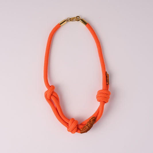 Neon orange rope necklace with accents of leather and  gold clasp on a light pink background