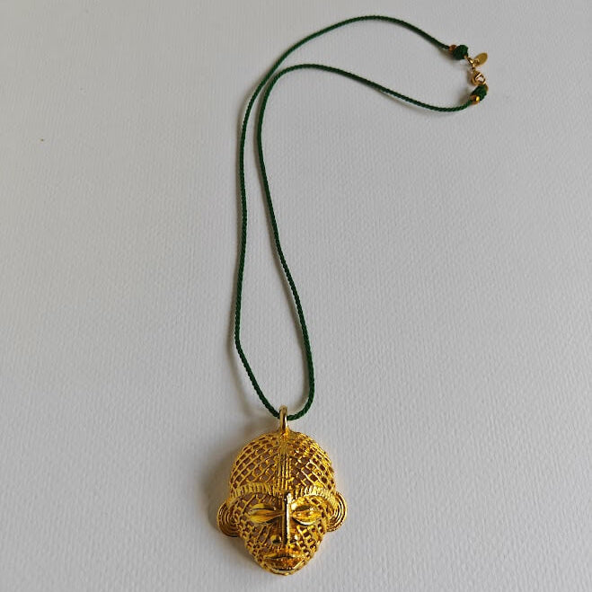 Gold pendant necklace on a green cord against a light gray background