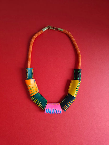 Neon orange rope and colourful geometric handcrafted leather beads necklace on a red background