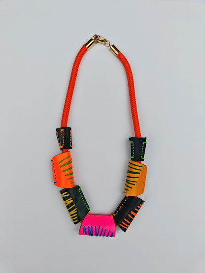 Neon orange rope and colourful geometric handcrafted leather beads necklace on a light gray background