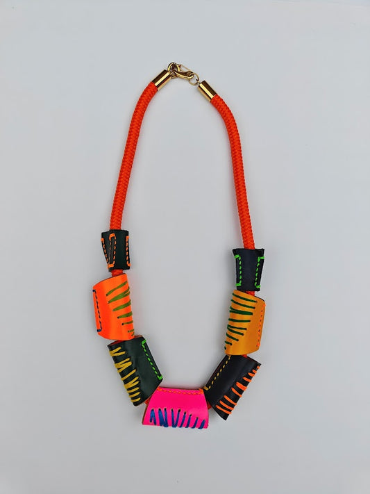 Neon orange rope and colourful geometric handcrafted leather beads necklace on a light gray background