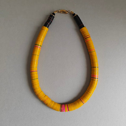 Yellow beaded necklace with black and pink accents on a gray background