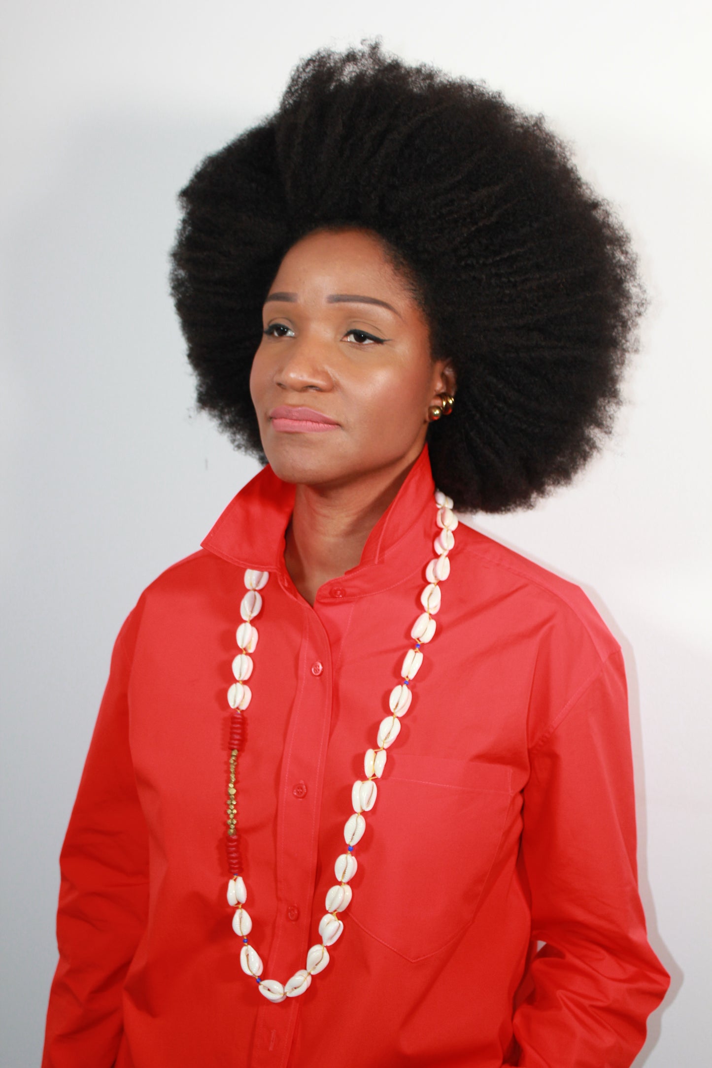 Person wearing a red outfit with a long cowrie shell necklace on a white background