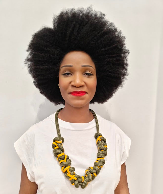Person with an afro wearing a chunky khaki green rope necklace, interwoven with yellow leather